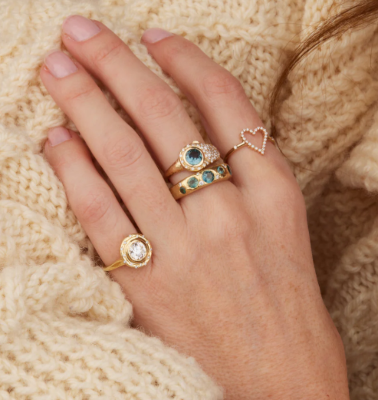 Hand wearing multiple gold rings with gemstones
